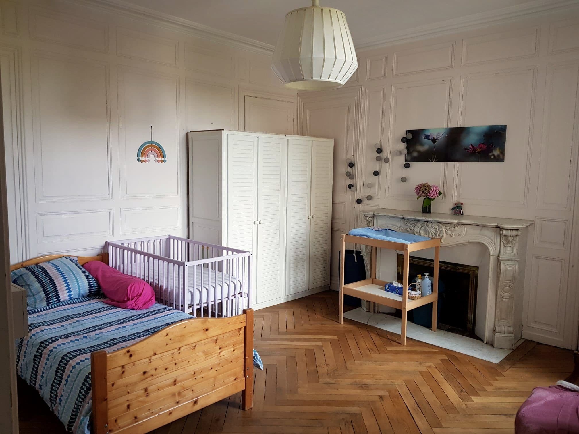Une chambre de la maison de Laval : un lit, un berceau, une table à langer et une cheminée ancienne.