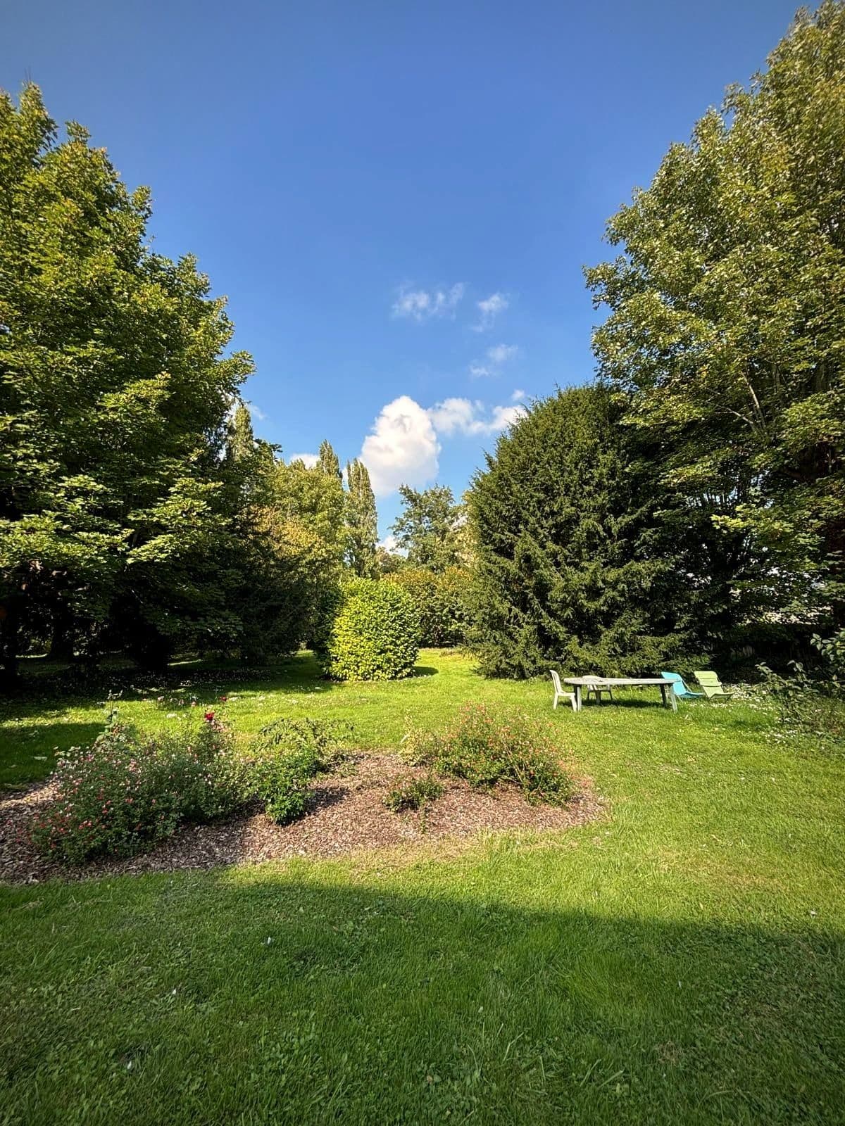 Le jardin arboré de Ligueil, avec sa pelouse, ses massifs fleuris et des transats à l’ombre.