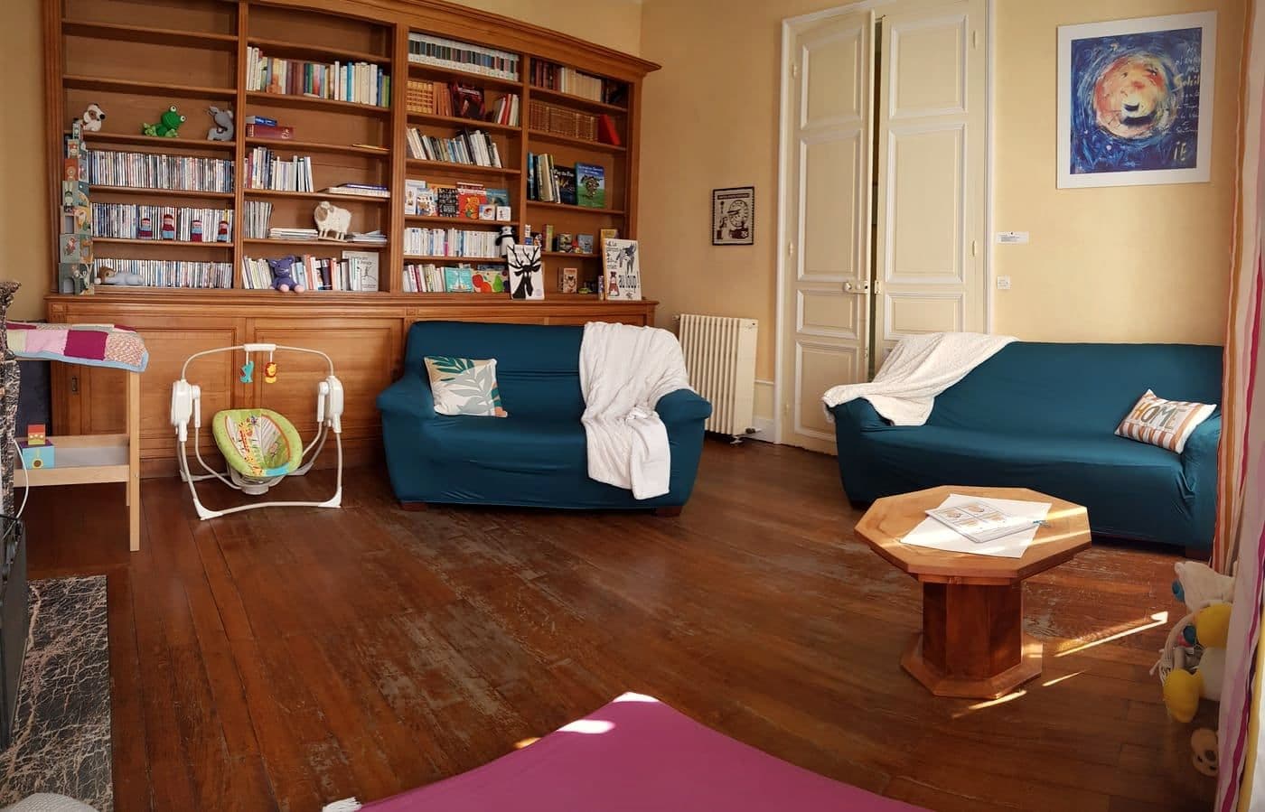 Le salon de la maison de Ligueil, avec sa bibliothèque murale, deux canapés et un transat de bébé.