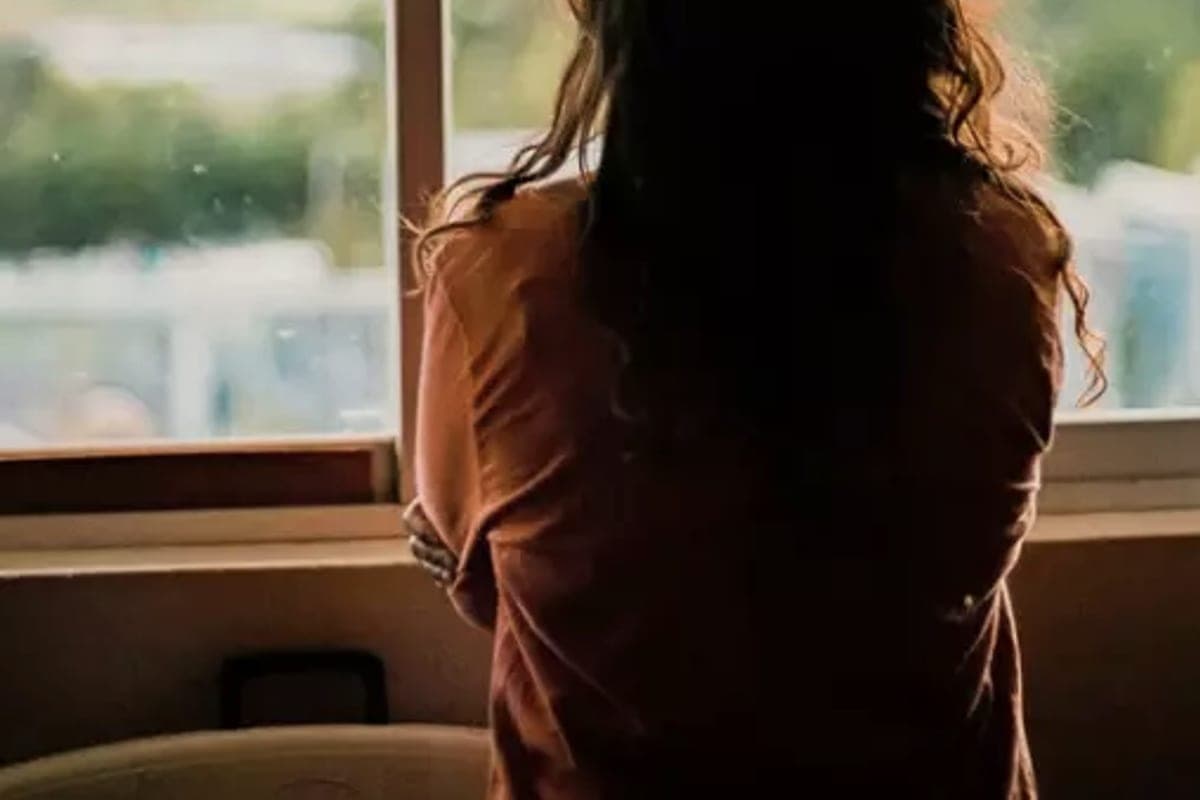 Une femme de dos, accoudée à une fenêtre ouverte sur un paysage de collines.