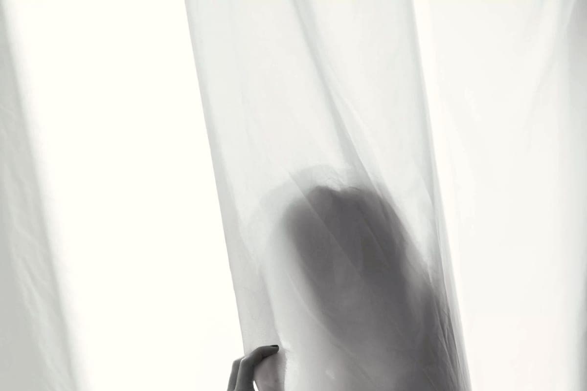La silhouette d’une femme enceinte, à contre-jour derrière un voilage.